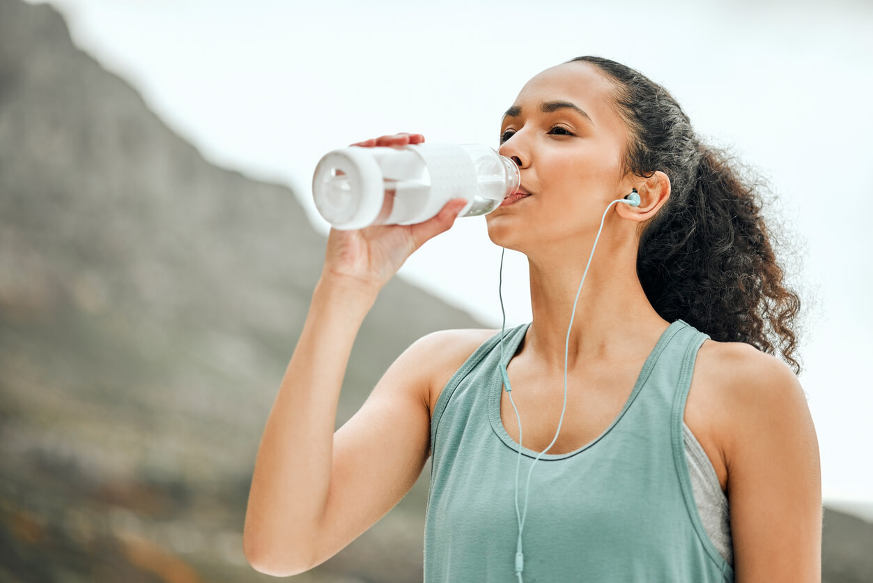 a woman wearing breathable materials and drinking water when it is too hot to be outside